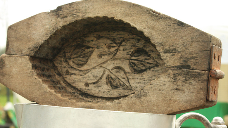 A wood butter mold has a leaf design carved onto the inside.