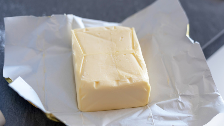 A brick of butter is unwrapped sitting on its wrapper.