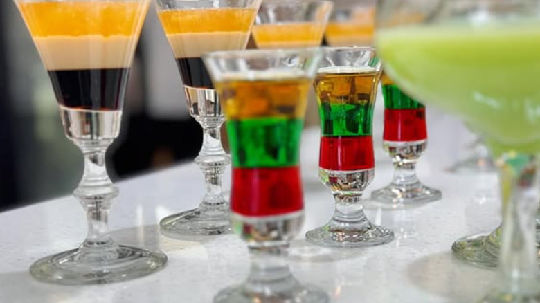 glasses of layered drinks with brown, beige and gold; orange, green and red; and plain light green.