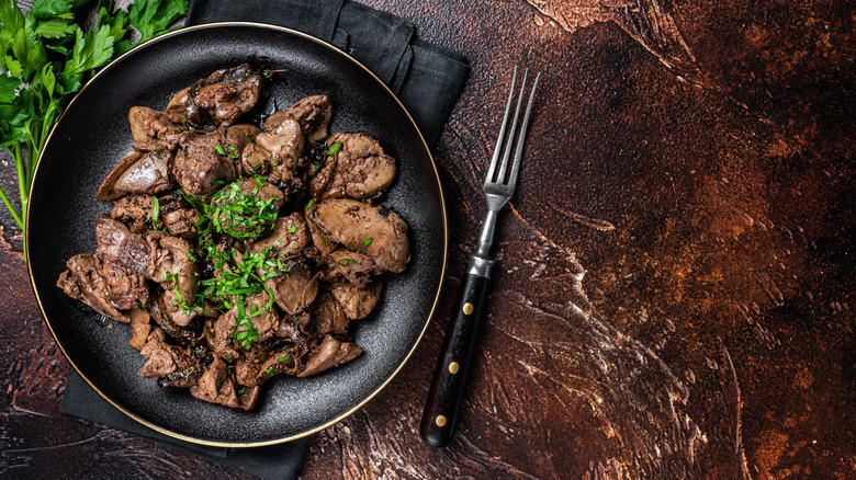 Cooked liver on a black plate next to a fork