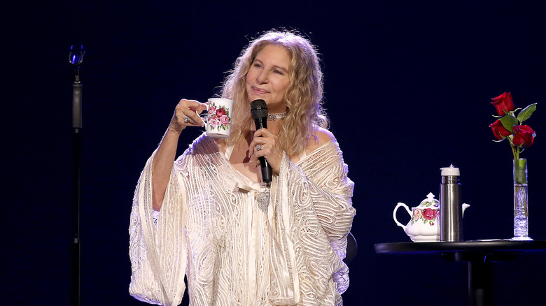 Barbara Streisand onstage holding a microphone and a mug, looking off into the distance