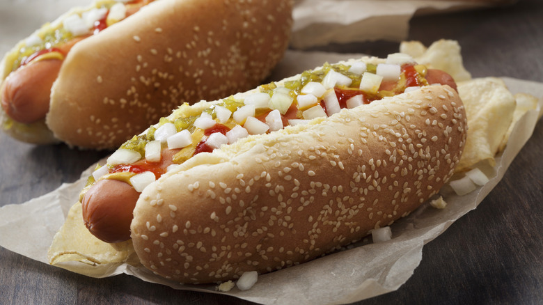 closeup of two hot dogs with various toppings in sesame seed buns