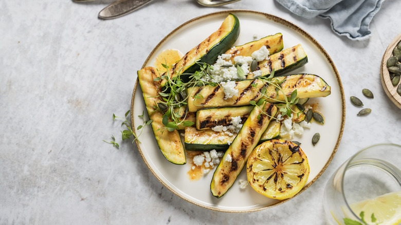 Grilled strips of zucchini on a plate with a grilled lemon, sprouts, and feta cheese