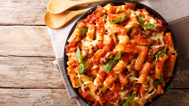 Baked ziti with basil on wood surface