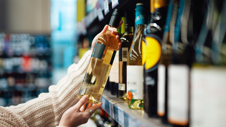 Person holds white wine bottle in wine aisle of store.