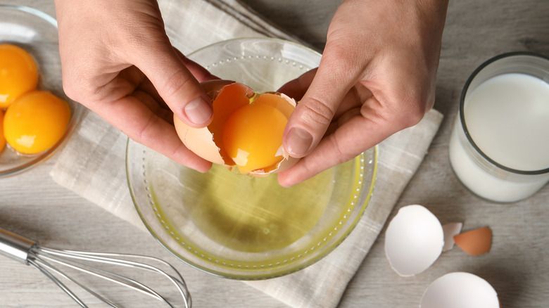 person cracking egg, separating egg yolk from egg white
