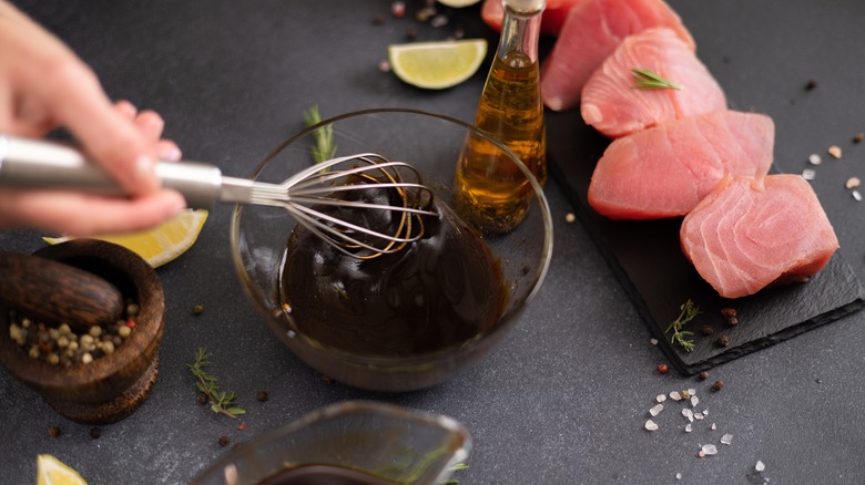 Person mixing a marinade in a glass blow next to pieces of raw tuna