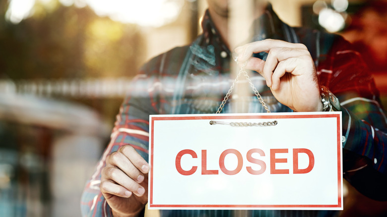 man hanging closed sign in business window