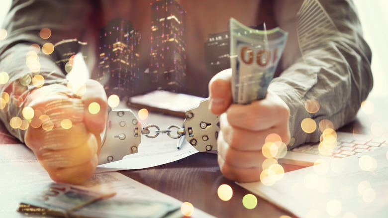 artsy bokeh photo, close-up of male executive's hands in handcuffs, holding cash