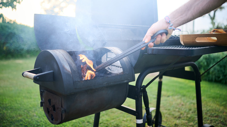 A person tends to the smoker with long tongs