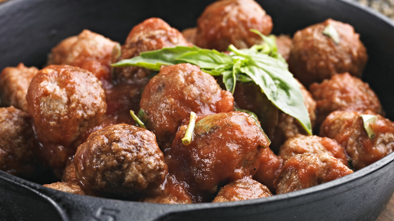 Meatballs in skillet covered in red sauce with a basil leaf
