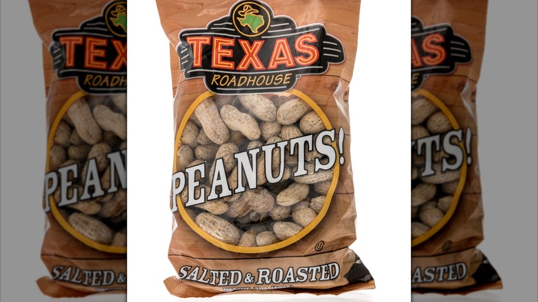 A bunch of salted peanuts are on a wooden straw plate.