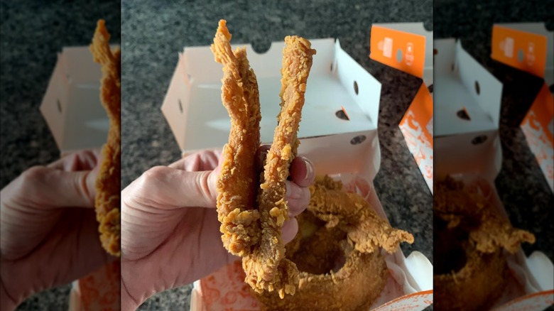 A hand holding 2 chicken tenders from Popeyes