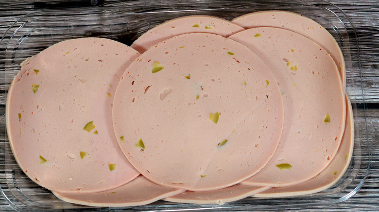 Sliced and speckled olive loaf deli meat on a clear plastic tray against a wooden backdrop