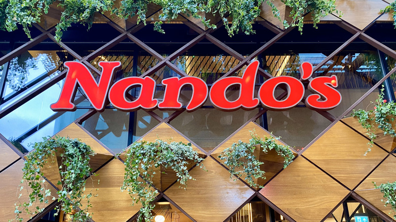 Exterior sign for Nando's surrounded by green potted plants