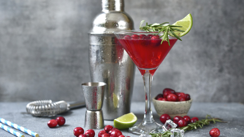 Cranberries cocktail with fresh lime in a martinil glass on a light grey slate, stone or concrete background.