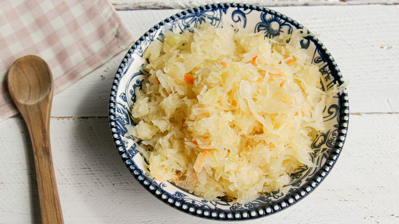Bowl of sauerkraut on a white table with a wooden spoon and checker-patterned cloth