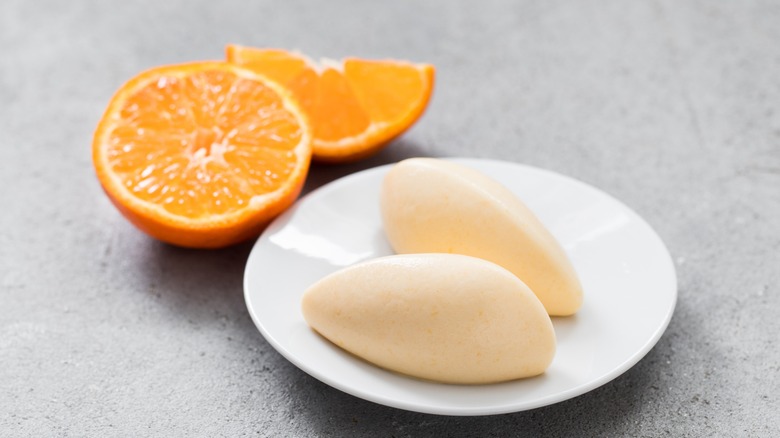 Two ice cream quenelles on a plate with a tangerine