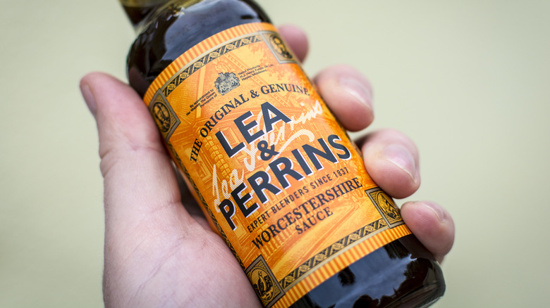 A hand holds a bottle of Worcestershire sauce