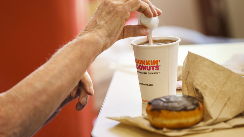 Customer pouring creamer Dunkin' coffee doughnut