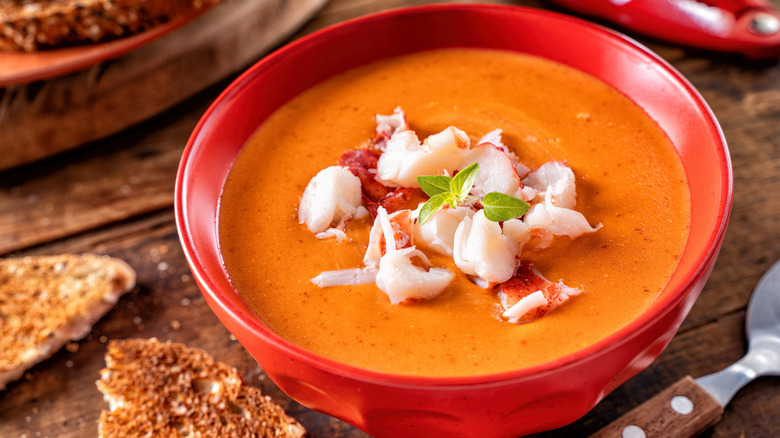 Bowl of lobster bisque in a red bowl next to toast
