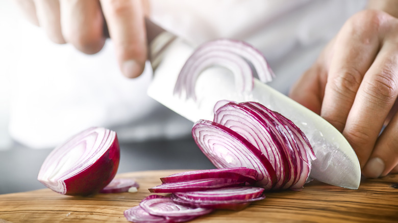 hand slicing red onions on cutting board