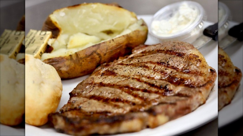 Plate of steak, baked potato, and roll with sour cream and butter on the side