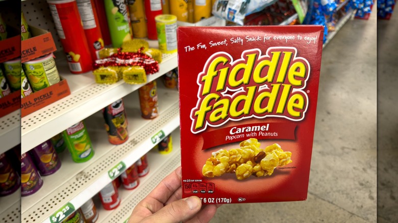 A hand holding a box of Fiddle Faddle Caramel popcorn in a store
