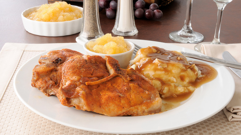 Plate of pork chops, apple sauce, and mashed potatoes on table.