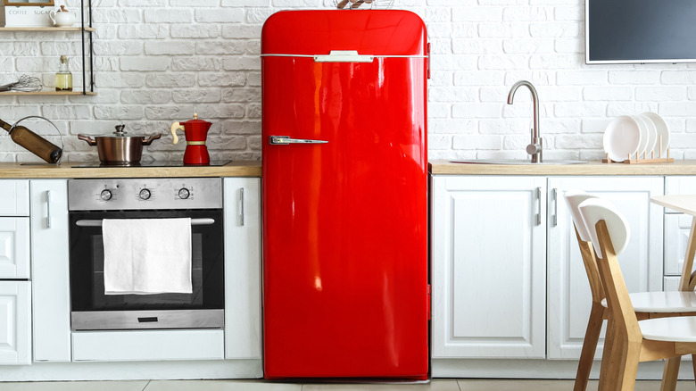 A red retro refrigerator stands out in the center of white cabinets, between the range and sink