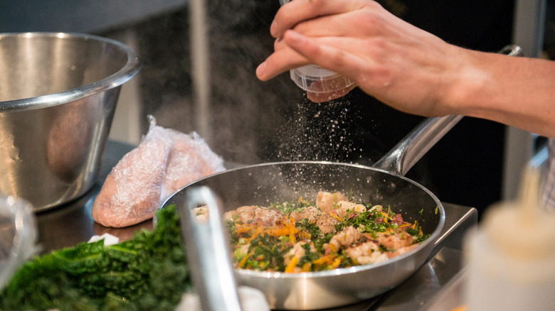 A chef sprinkling seasoning into a frying pan