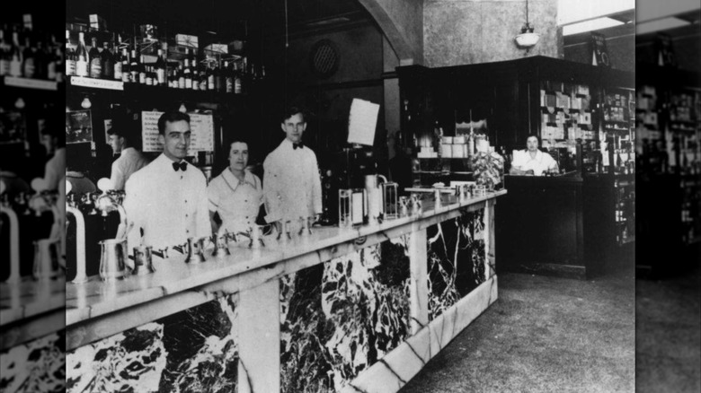 A black-and-white photo of the first Howard Johnson's location, showing three people standing behind a counter at a soda fountain
