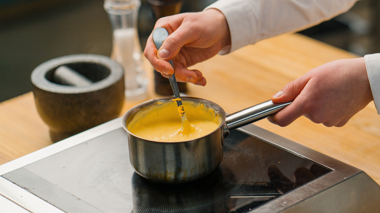 Chef stirring small saucepan of cheese sauce.