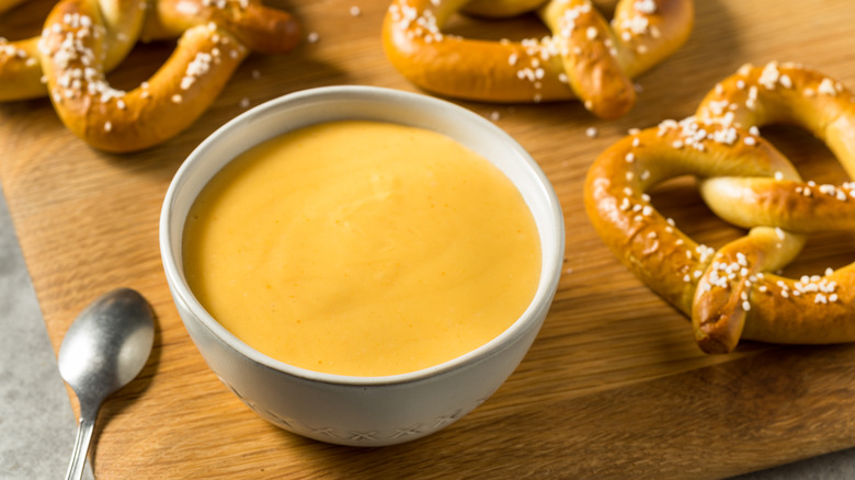 Bowl of beer cheese dip with Bavarian pretzels on wooden cutting board.