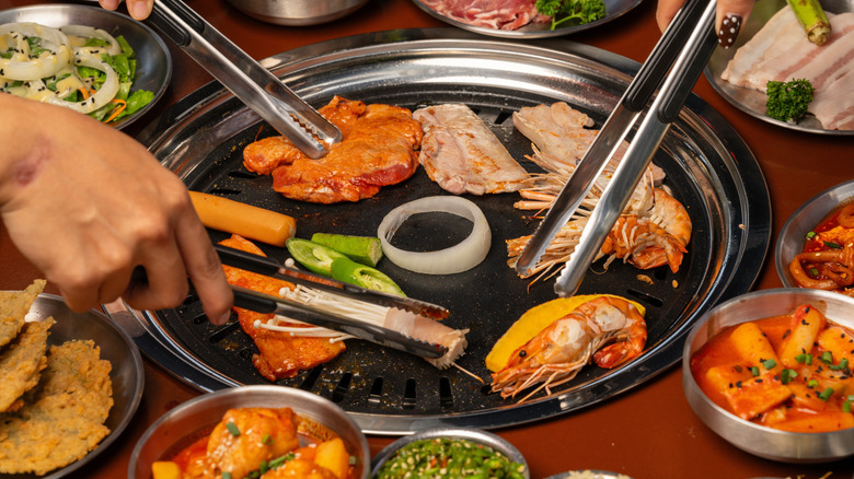 Three hands holding tongs on a grill of meat and shrimp