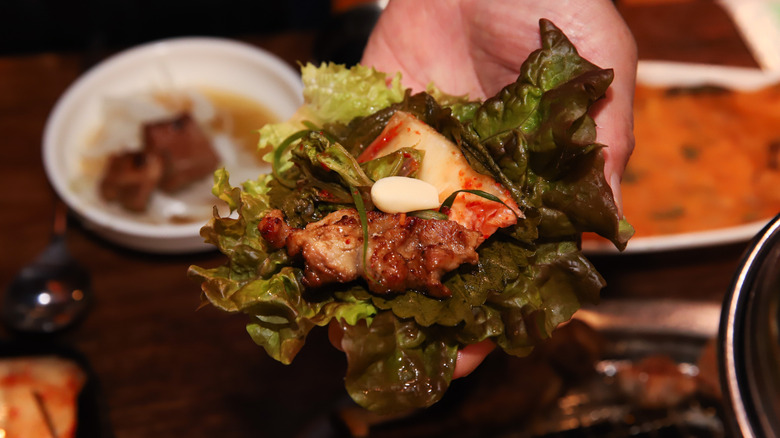 Hand holding lettuce ssam with meat