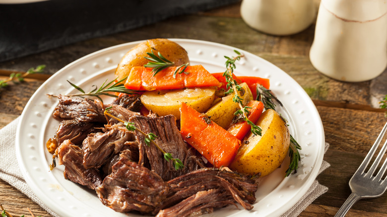 Plate of pot roast with potatoes and carrots on a wooden table