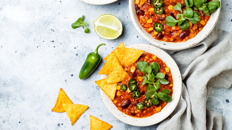 bowls of vegetarian chili with beans, tortilla chips, lime, jalapeno