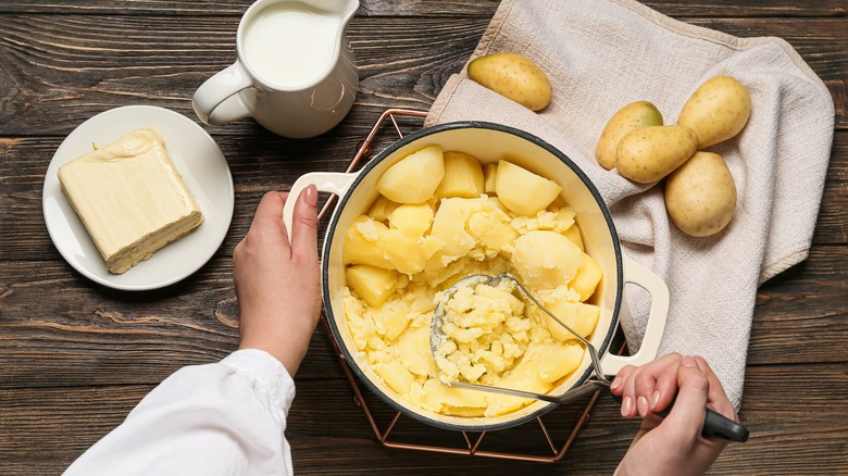 Hand mashing potatoes in bowl with ingredients around it