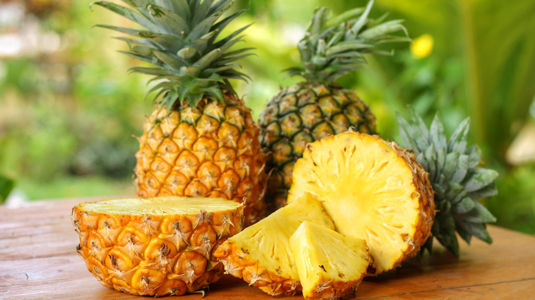 Whole and cut pineapples on a wooden surface