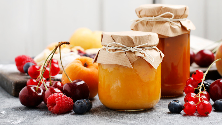 Jam jars with cherries, red currants, and berries alongside