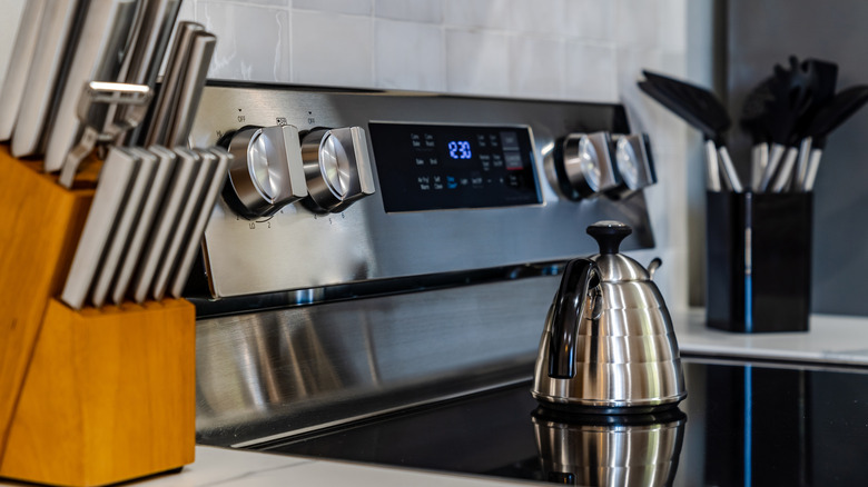 Stainless steel kitchen kettle on glass stovetop next to wooden knife block