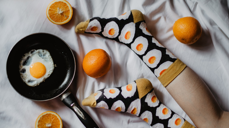 egg in pan on bed with oranges and legs in socks