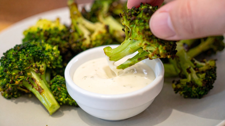Hand dipping roasted broccoli in sauce