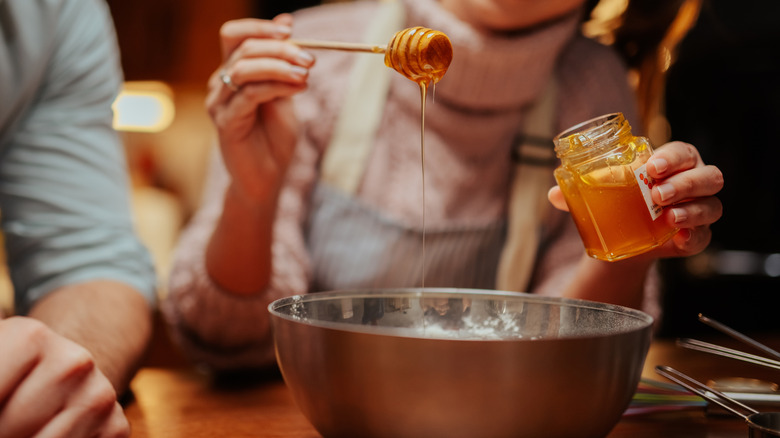 A woman's hands adding honey to a metal mixing bowl