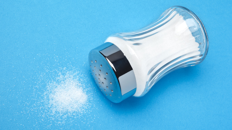 Salt shaker on blue background with spilled salt