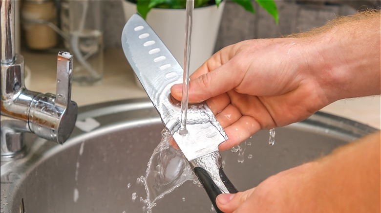 Hands running knife under water 