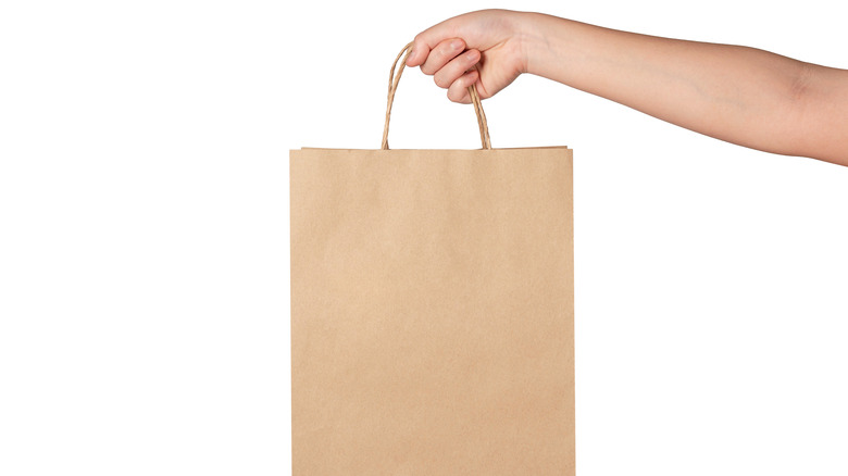 Holding a brown paper bag with handles 