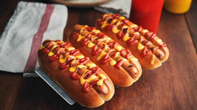 Three hot dogs with mustard and ketchup on a picnic table