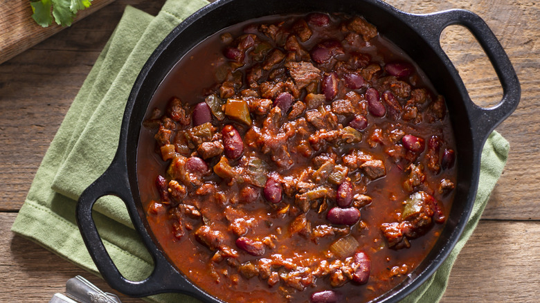 overhead shot of homemade chili con carne in a cast iron pot on a wooden table
